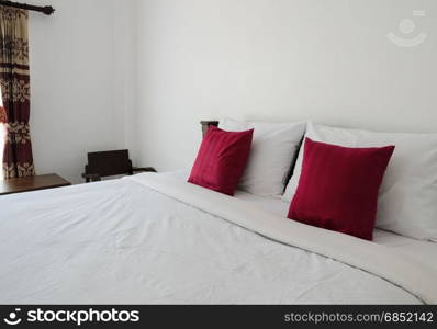 White bedroom with tidy King size bed and red pillows