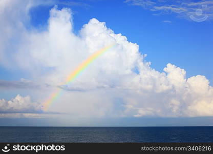 white big clouds and multi-coloured rainbow over sea in afternoon