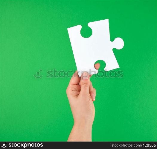 white big puzzle in female hand on green background, business concept, copy space