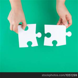 white big puzzles in female hand on green background, copy space