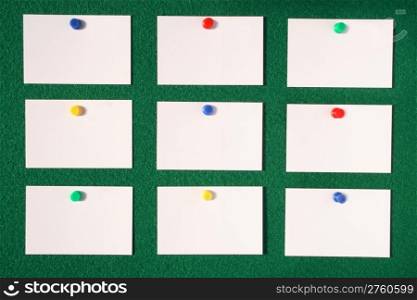 White blank business/advertisement cards pinned to a green felt notice board.