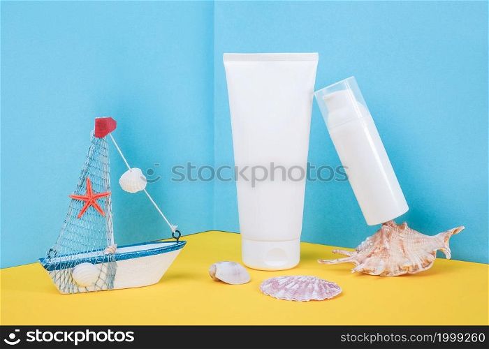 White blank cosmetic tube, bottle with sunscreen, sun cream, moisturizing lotion, seashells and small boat on blue, yellow background. Concept skin care in sea beach holidays in summer vacation.. White blank cosmetic tube, bottle with sunscreen, sun cream, moisturizing lotion, seashells and small boat on blue, yellow background. Concept skin care in sea beach holidays in summer vacation