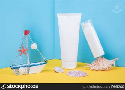 White blank cosmetic tube, bottle with sunscreen, sun cream, moisturizing lotion, seashells and small boat on blue, yellow background. Concept skin care in sea beach holidays in summer vacation.. White blank cosmetic tube, bottle with sunscreen, sun cream, moisturizing lotion, seashells and small boat on blue, yellow background. Concept skin care in sea beach holidays in summer vacation