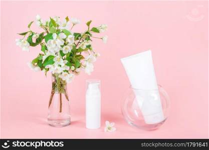 White blank cosmetics tube and bottle and apple blooming branch in vase on pink background. Natural Organic Spa Cosmetic Beauty Concept. Mockup Front view.. White blank cosmetics tube and bottle and apple blooming branch in vase on pink background. Natural Organic Spa Cosmetic Beauty Concept. Mockup Front view