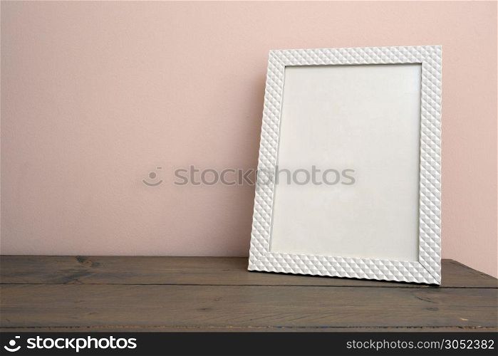 White blank mock up of photo frame on the light background. Home interior, wooden shelf near pink wall close-up. White blank mock up of photo frame on the light background. Home interior, wooden shelf near pink wall