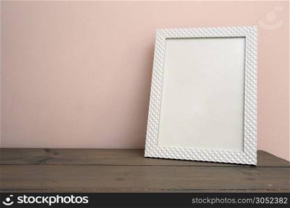 White blank mock up of photo frame on the light background. Home interior, wooden shelf near pink wall close-up. White blank mock up of photo frame on the light background. Home interior, wooden shelf near pink wall