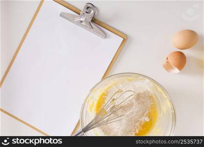 white blank paper clipboard with whipped egg flour bowl white backdrop