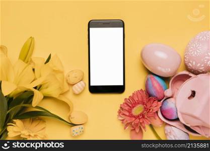 white blank screen mobile phone decorated with lily gerbera flower colorful easter eggs yellow background