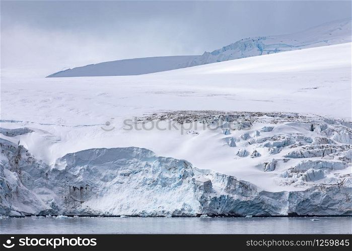 White blue glacier tongue falls directly into the calm sea of Antarctica