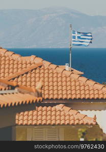 White blue state flag of Greece on roof of private estate, tourist house in seaside Mediterranean town.. Greek flag on roof top of home