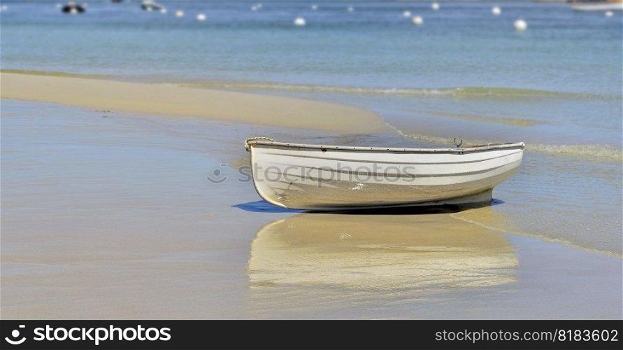 white boat placed on the sand near the blue sea with reflection on the wet sand 