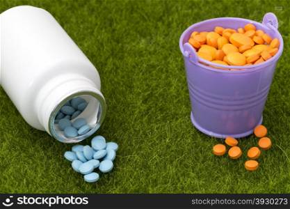 White bottle of blue pills and buckets filled with orange tablets. White bottle of blue pills and buckets filled with orange tablets on the green grass