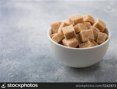 White bowl of natural brown sugar cubes on light background.