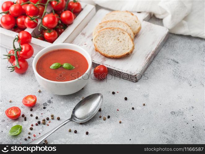 White bowl plate of creamy tomato soup with spoon on light background with box of raw tomatoes and bread. Space for text