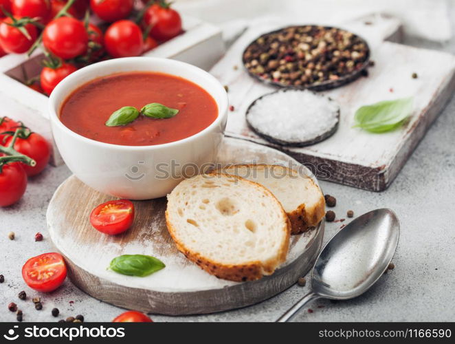 White bowl plate of creamy tomato soup with spoon on light background with box of raw tomatoes and bread. Space for text