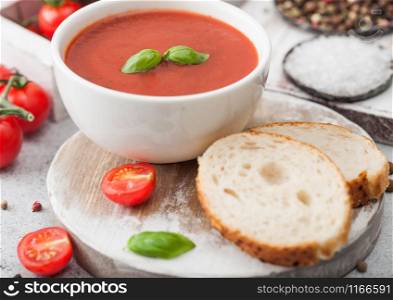 White bowl plate of creamy tomato soup with spoon on light background with box of raw tomatoes and bread. Macro
