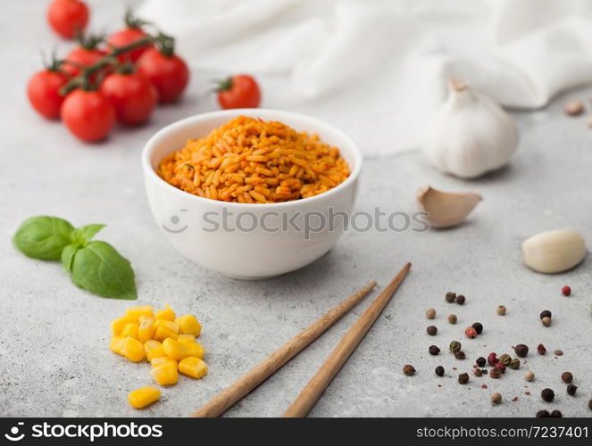 White bowl plate with boiled red long grain basmati rice with vegetables on light background with sticks and tomatoes with corn,garlic and basil.