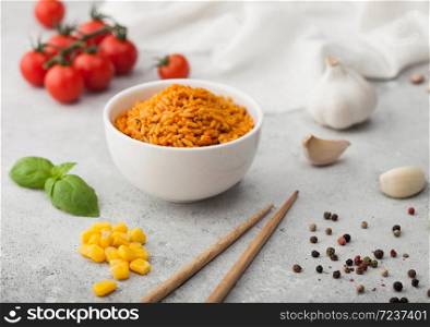 White bowl plate with boiled red long grain basmati rice with vegetables on light background with sticks and tomatoes with corn,garlic and basil.