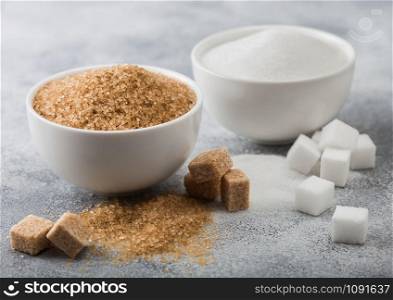 White bowl plates of natural brown and white refined sugar and cubes on light background.