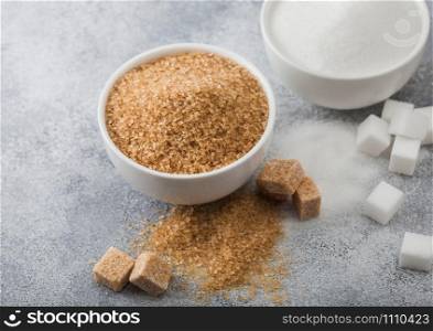 White bowl plates of natural brown and white refined sugar and cubes on light background.