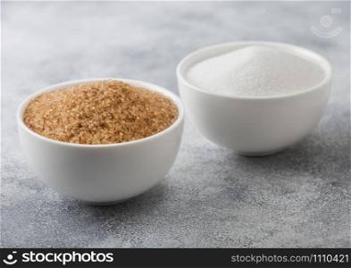 White bowl plates of natural brown and white refined sugar on light background.