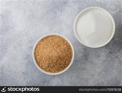 White bowl plates of natural brown and white refined sugar on light background. Top view
