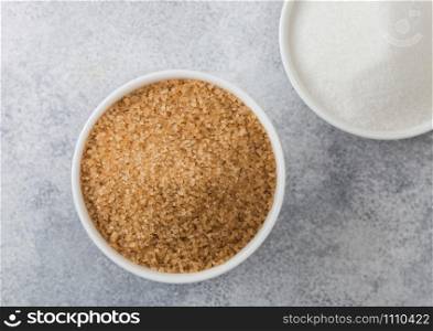 White bowl plates of natural brown and white refined sugar on light background. Top view