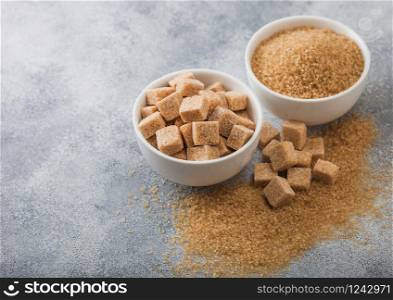 White bowl plates of natural brown sugar cubes and refined sugar on light background.