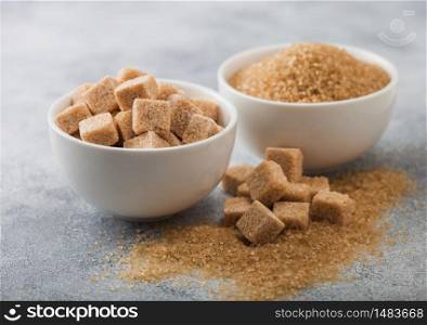 White bowl plates of natural brown sugar cubes and refined sugar on light background.