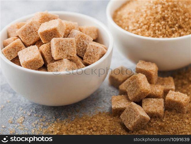 White bowl plates of natural brown sugar cubes and refined sugar on light background. Macro