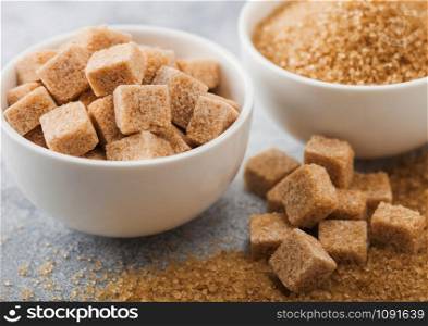 White bowl plates of natural brown sugar cubes and refined sugar on light background. Macro