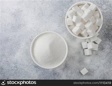 White bowl plates of natural white sugar cubes and refined sugar on light background. Top view