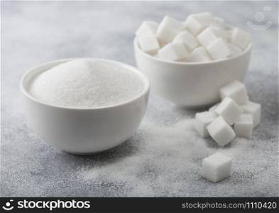 White bowl plates of natural white sugar cubes and refined sugar on light background.