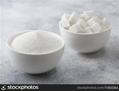 White bowl plates of natural white sugar cubes and refined sugar on light background. Top view