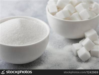 White bowl plates of natural white sugar cubes and refined sugar on light background.