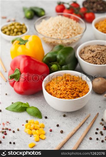 White bowl plates with boiled long grain basmati rice with vegetables and mushrooms on light background with sticks and paprika pepper with corn,garlic and basil with tomatoes and peas.