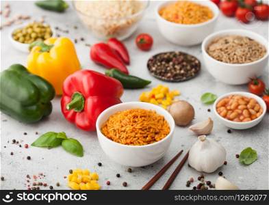 White bowl plates with boiled long grain basmati rice with vegetables and mushrooms on light background with sticks and paprika pepper with corn,garlic and basil with beans and peas.