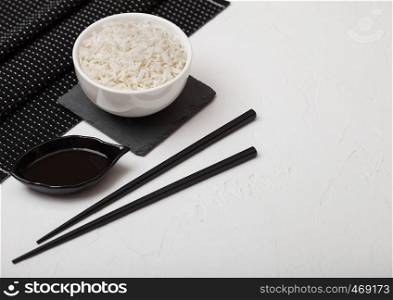 White bowl with boiled organic basmati jasmine rice with black chopsticks and sweet soy sauce on bamboo place mat on white background.
