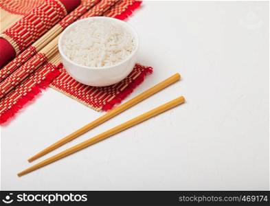 White bowl with boiled organic basmati jasmine rice with wooden chopsticks and sweet soy sauce on bamboo placemat with red linen towel on black stone.