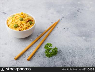 White bowl with boiled organic basmati vegetable rice with wooden chopsticks on light background. Yellow corn and green peas with paprika slices.