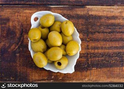 White bowl with boned green olives on a wooden background