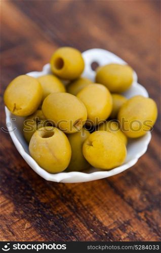 White bowl with boned green olives on a wooden background