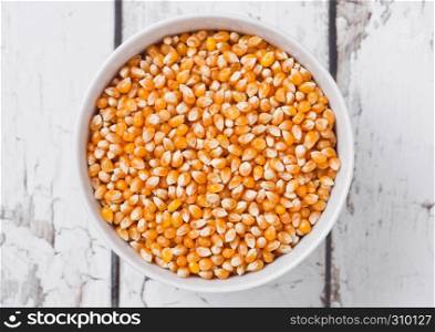 White bowl with raw sweet corn and popcorn on wooden background