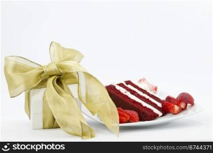 White box wrapped with gold ribbon is a special gift placed next to a slice of red velvet cake garnished with sliced strawberries