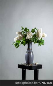 White branches of lilac in vase on gray background. Spring branch of blooming lilac on the table with gray background. Fallen lilac flowers on the table.