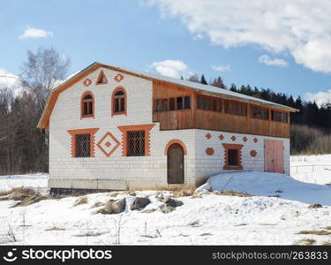 White brick cottage at the forest edge, snow covered area, early spring