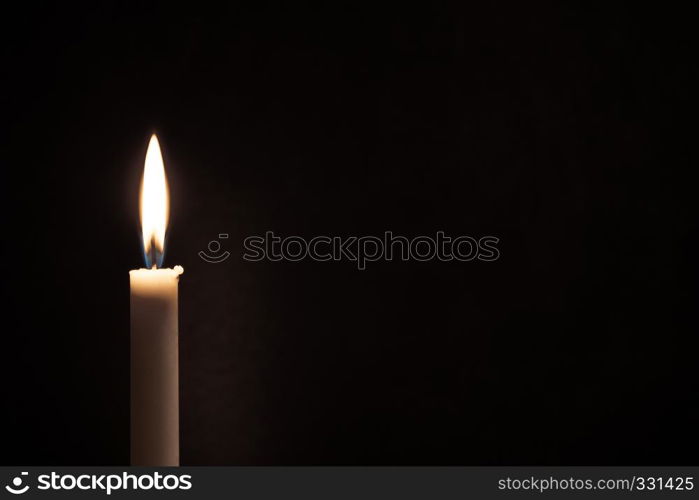 White burning candle burns on a black background. Mourning, sadness, sorrow. Located on the left. Empty space for text.. White burning candle on a black background. Mourning, burning candle.