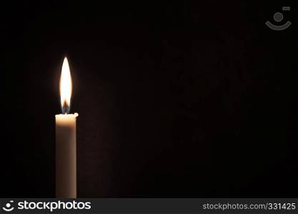 White burning candle burns on a black background. Mourning, sadness, sorrow. Located on the left. Empty space for text.. White burning candle on a black background. Mourning, burning candle.