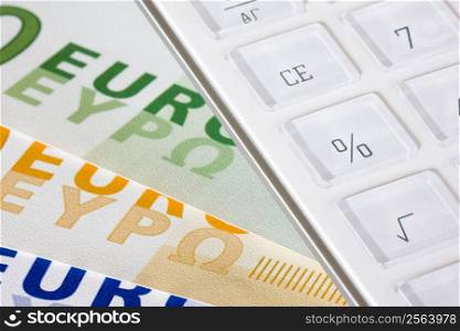 White calculator lying on euro banknotes. Focus on the percentage symbol