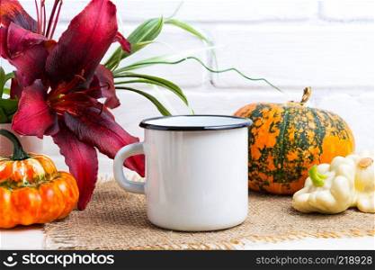 White campfire enamel coffee mug mockup with Thanksgiving fall orange pumpkin and red lily.  Empty mug mock up for design promotion. 
